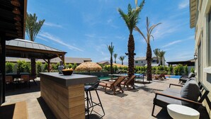Eine Außenpatio mit Bar, Liegestühlen, einem Pool und Palmen.