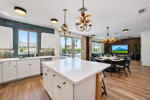Une cuisine moderne dotée d’un grand îlot central, de luminaires suspendus et offrant une vue sur l’extérieur.
