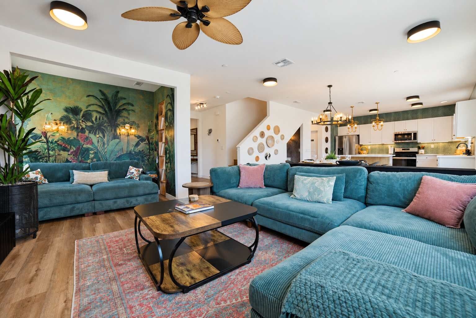A modern living room with a large sofa set, a coffee table, and a tropical-themed mural.