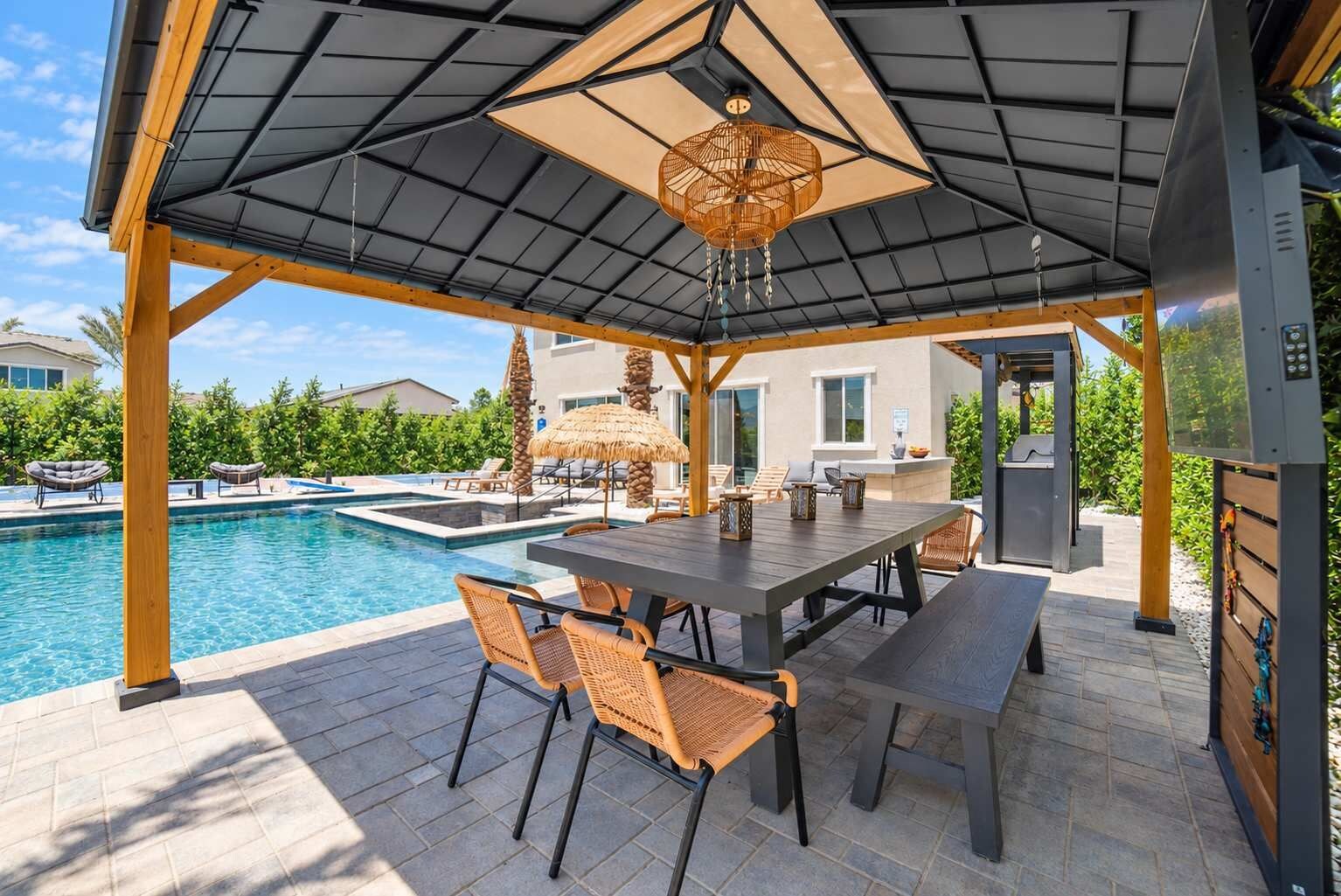 A covered outdoor area with a pool, a table with chairs, and a pergola structure.