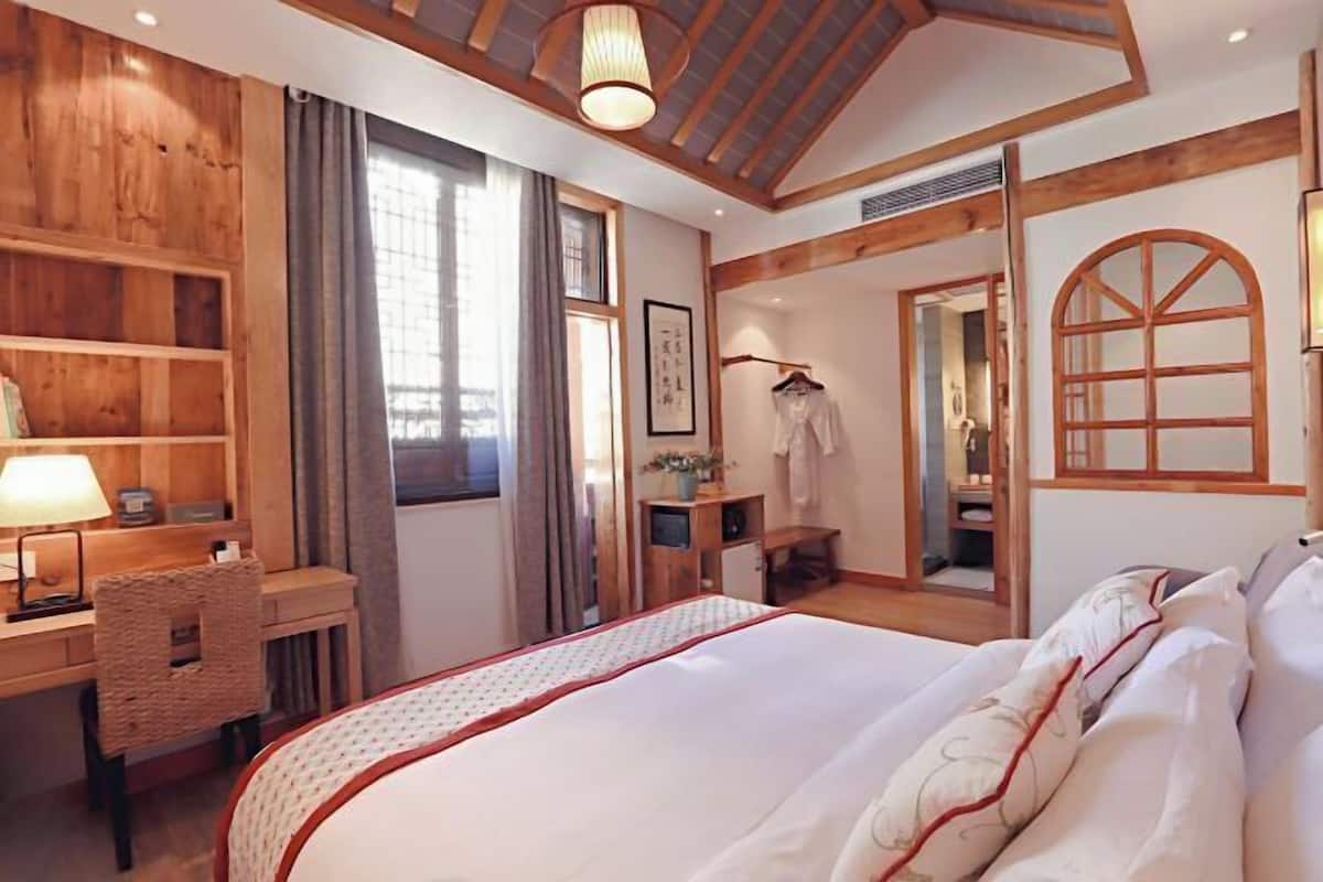 A hotel room with a large bed, wooden walls, a desk with a lamp, and a wardrobe.