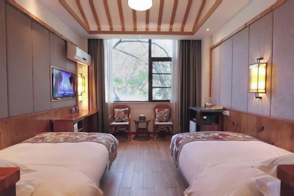 A hotel room with two beds, a TV, a small table, chairs, and a window with a view.