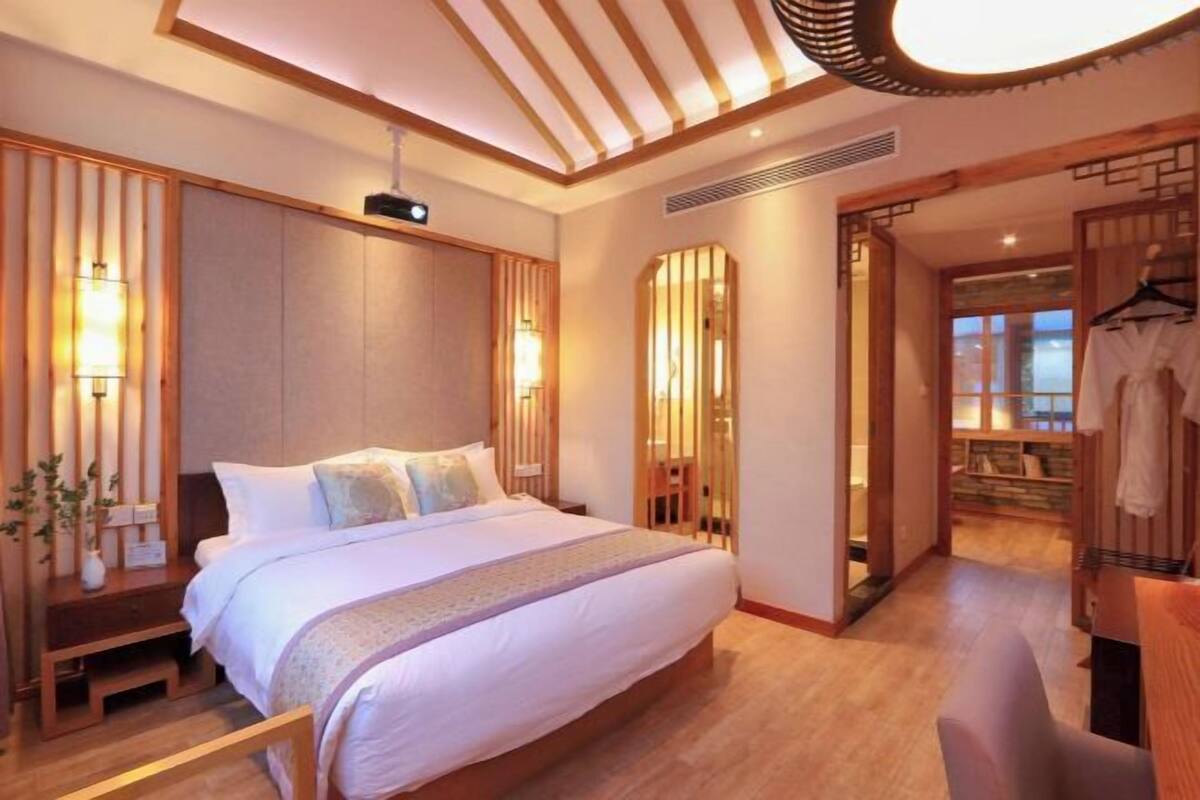 A modern hotel room with a large bed, wooden paneling, and a view of the outdoor area.