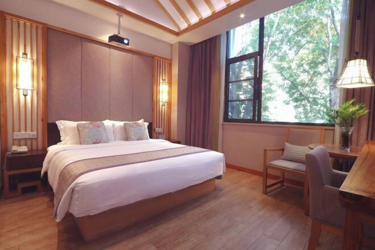 A bedroom with a large bed, bedside tables, a desk, and a window with a view of trees.