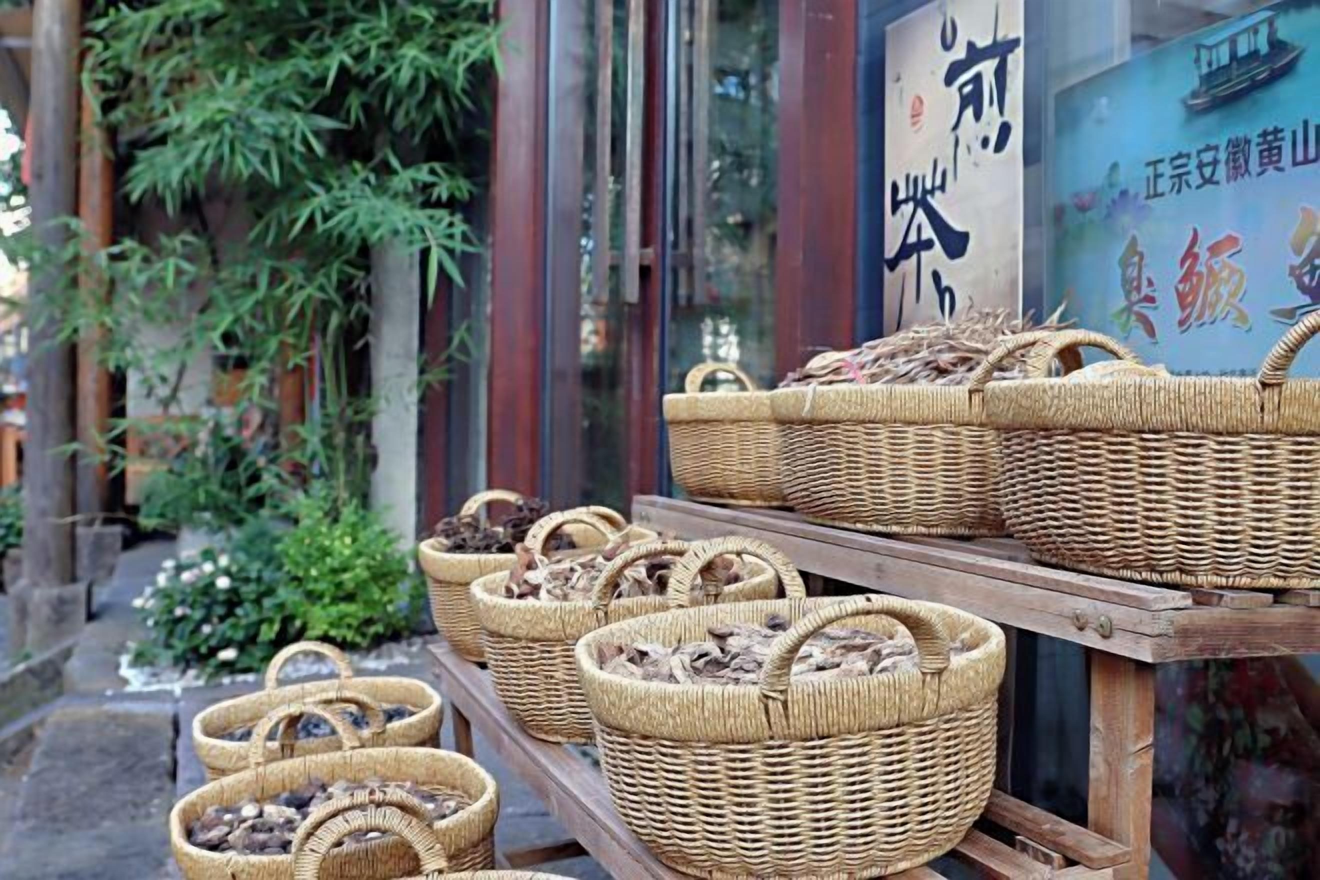 Cestas de mimbre llenas de setas secas expuestas frente a un edificio con caracteres chinos tradicionales en la pared.