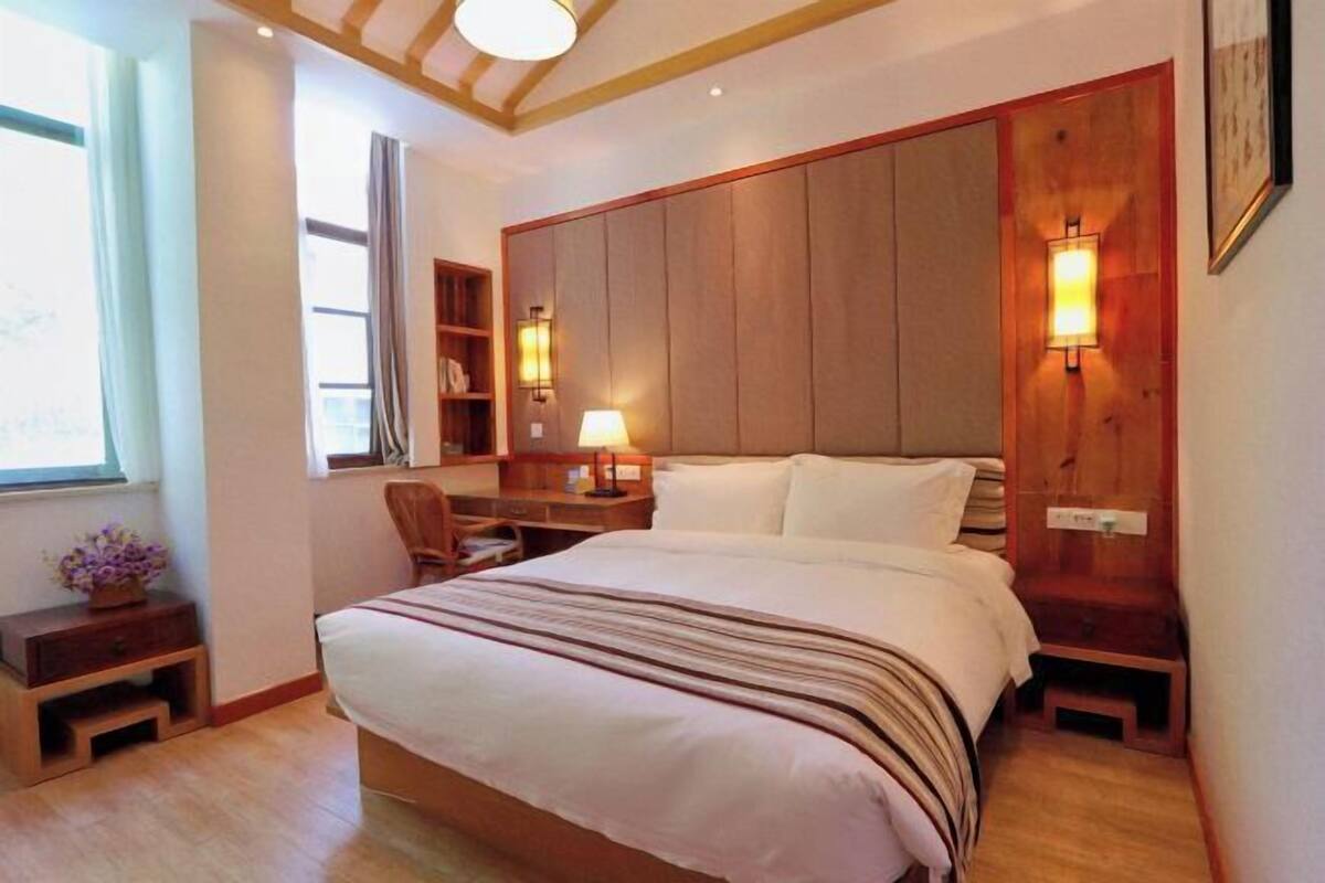 A bedroom with a large bed, wooden headboard, bedside lamps, a nightstand, a desk, and a chair.