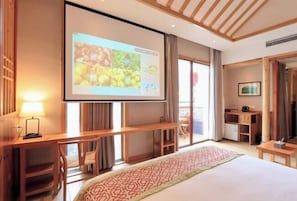 A hotel room with a large bed, a desk with a lamp, a TV screen, and a balcony with a view.