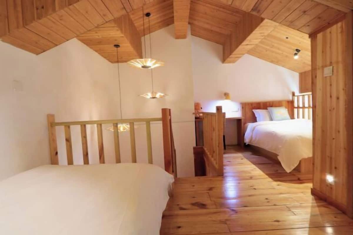 A wooden cabin with two beds, a staircase, and a wooden ceiling.