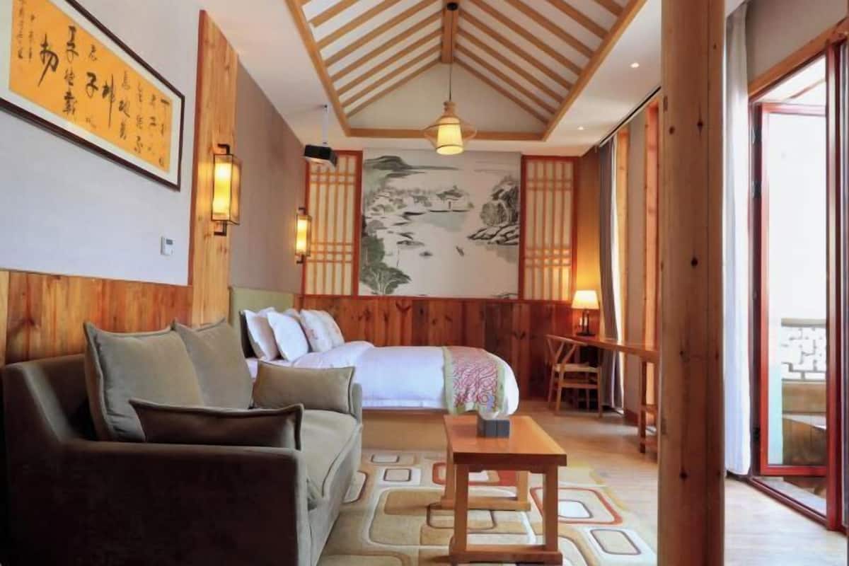 A room with a bed, a sofa, a table, and a painting on the wall.