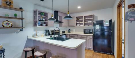A modern kitchen with a central island, bar stools, pendant lighting, and built-in cabinetry.