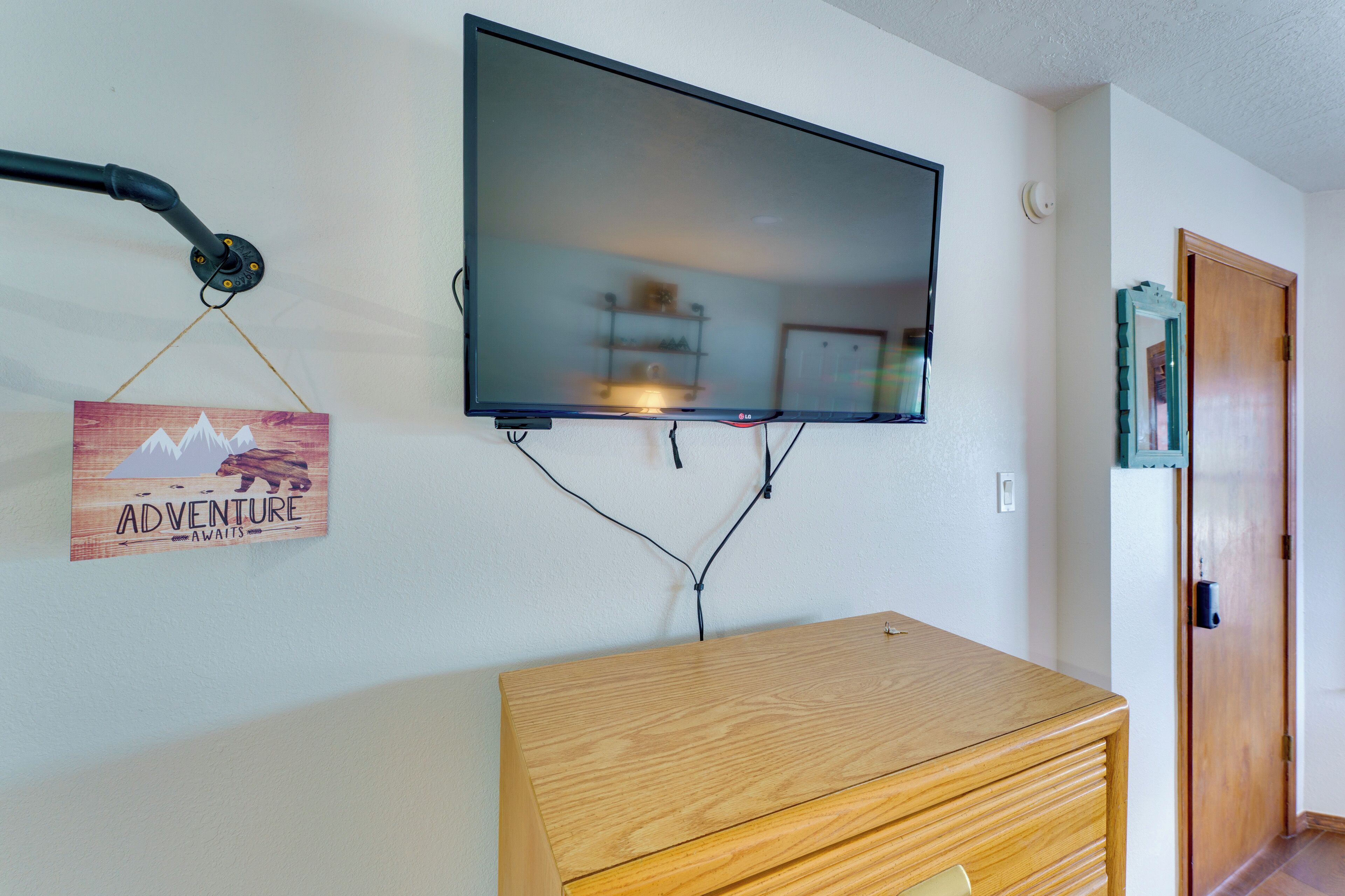 A flat-screen TV mounted on a wall, a wooden dresser below, and a door to the right.
