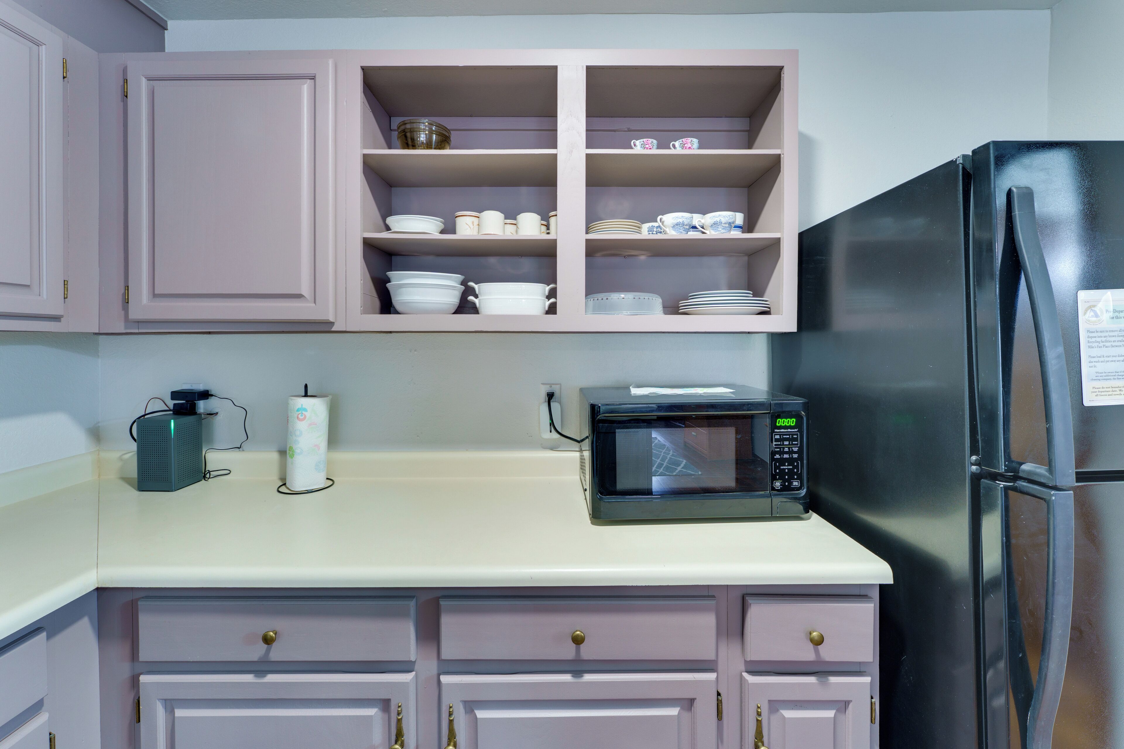 A kitchen with a microwave, a refrigerator, and pink cabinets.