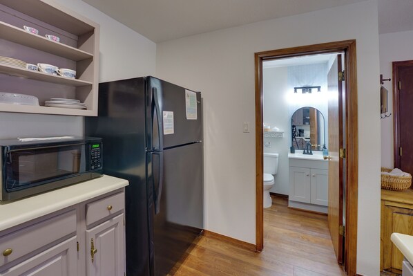 A compact kitchen with a black refrigerator, a microwave, and a shelf with dishes. - Mtn Views: Waterfront Red River Studio (Red River)