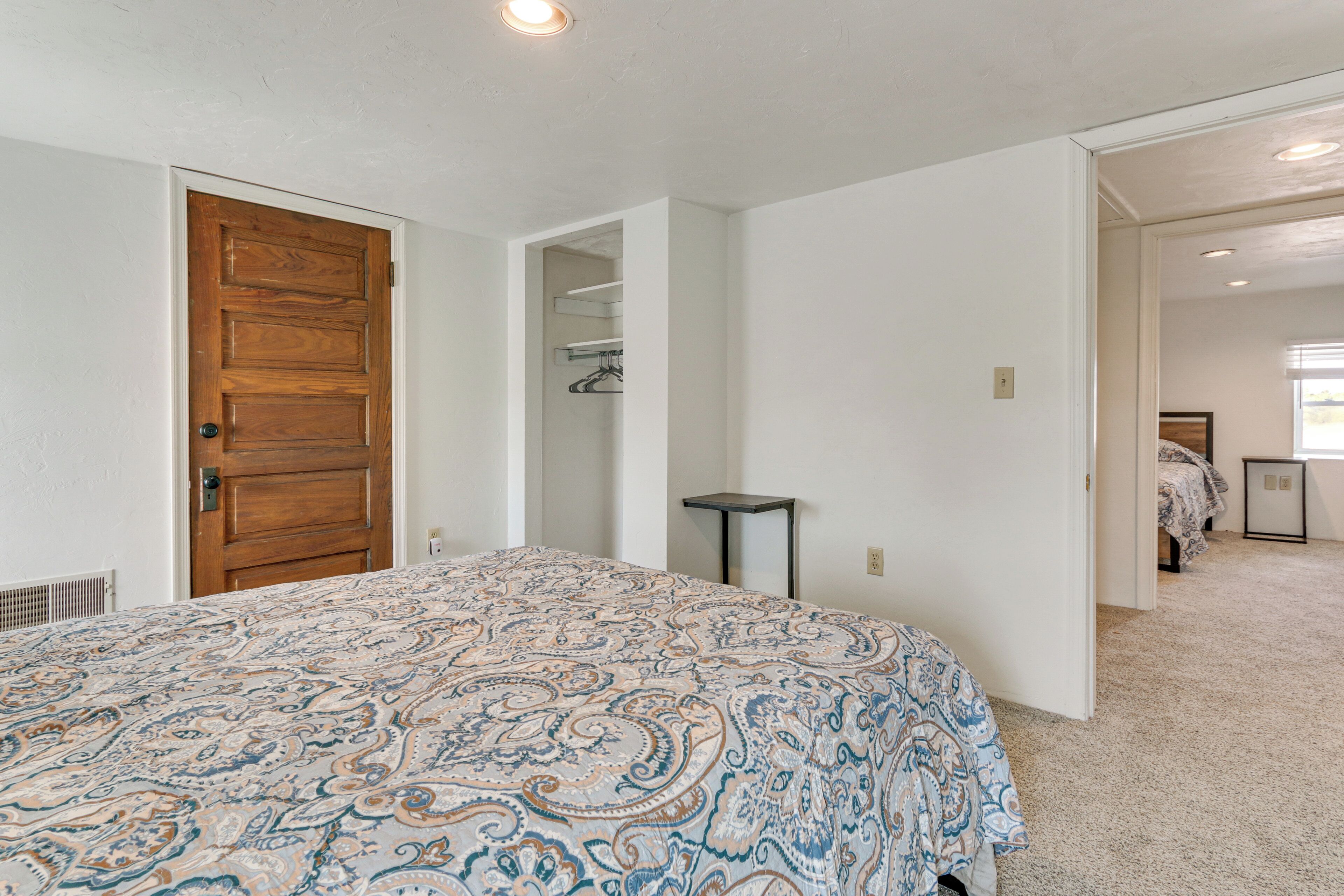 A bedroom with a large bed, a wooden door, a small table, and a closet with shelves.