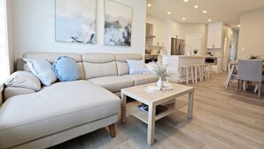 Ein modernes Wohnzimmer mit einem beigefarbenen Ecksofa, einem Holztisch und abstrakter Wandkunst.