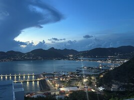 A coastal town at dusk with a marina, buildings, and mountains in the background.