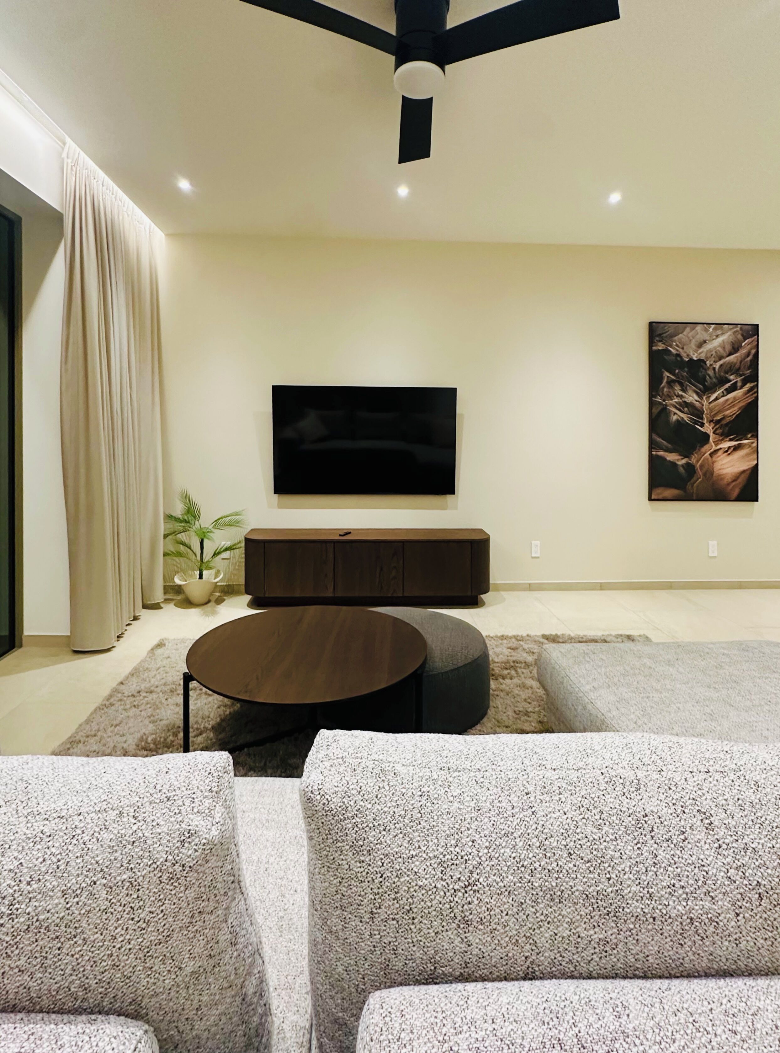 A modern living room with a flat-screen TV mounted on the wall, a dark wooden coffee table, and two grey sofas.