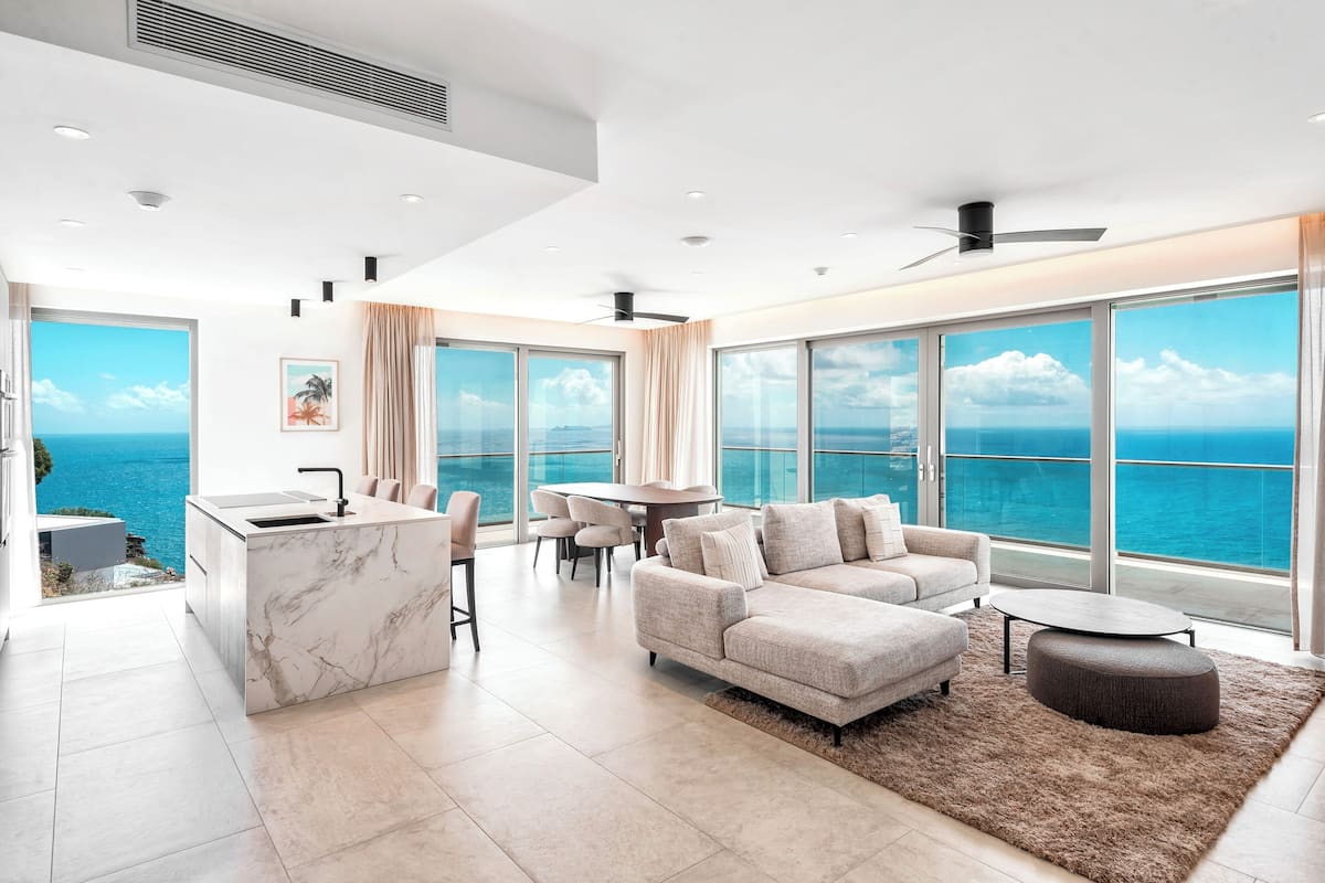 Una sala de estar moderna con un gran ventanal, una isla de cocina de mármol, un sofá y un comedor.