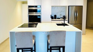 Une cuisine moderne dotée d’un îlot central, de deux tabourets de bar, d’appareils électroménagers intégrés et d’un éclairage encastré.