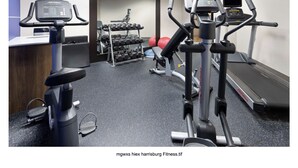Une salle de sport équipée de machines de cardio, d’haltères et d’un ballon d’exercice rouge.