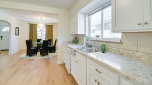 A modern kitchen with white cabinets, a marble countertop, and a dining area with a round table and chairs. - Walk to Ritter Park: Renovated Home Near Marshall! (Huntington)
