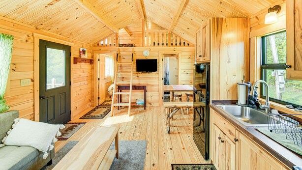 A wooden cabin interior with a kitchen, dining area, and a living room with a sofa and a TV. - 5 Mi to Susquehanna Boating! Secluded Log Cabin (Winfield)