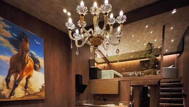 A modern living room with a chandelier, a sofa, a coffee table, and a painting of a horse. - The HH Point (Tirana)