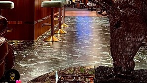 A bar area with wooden bar counters, bar stools, and a large decorative sculpture. - The HH Point (Tirana)
