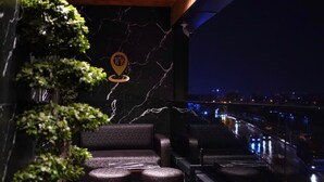A rooftop terrace with a view of the city at night, featuring a marble wall, a potted plant, and seating area. - The HH Point (Tirana)