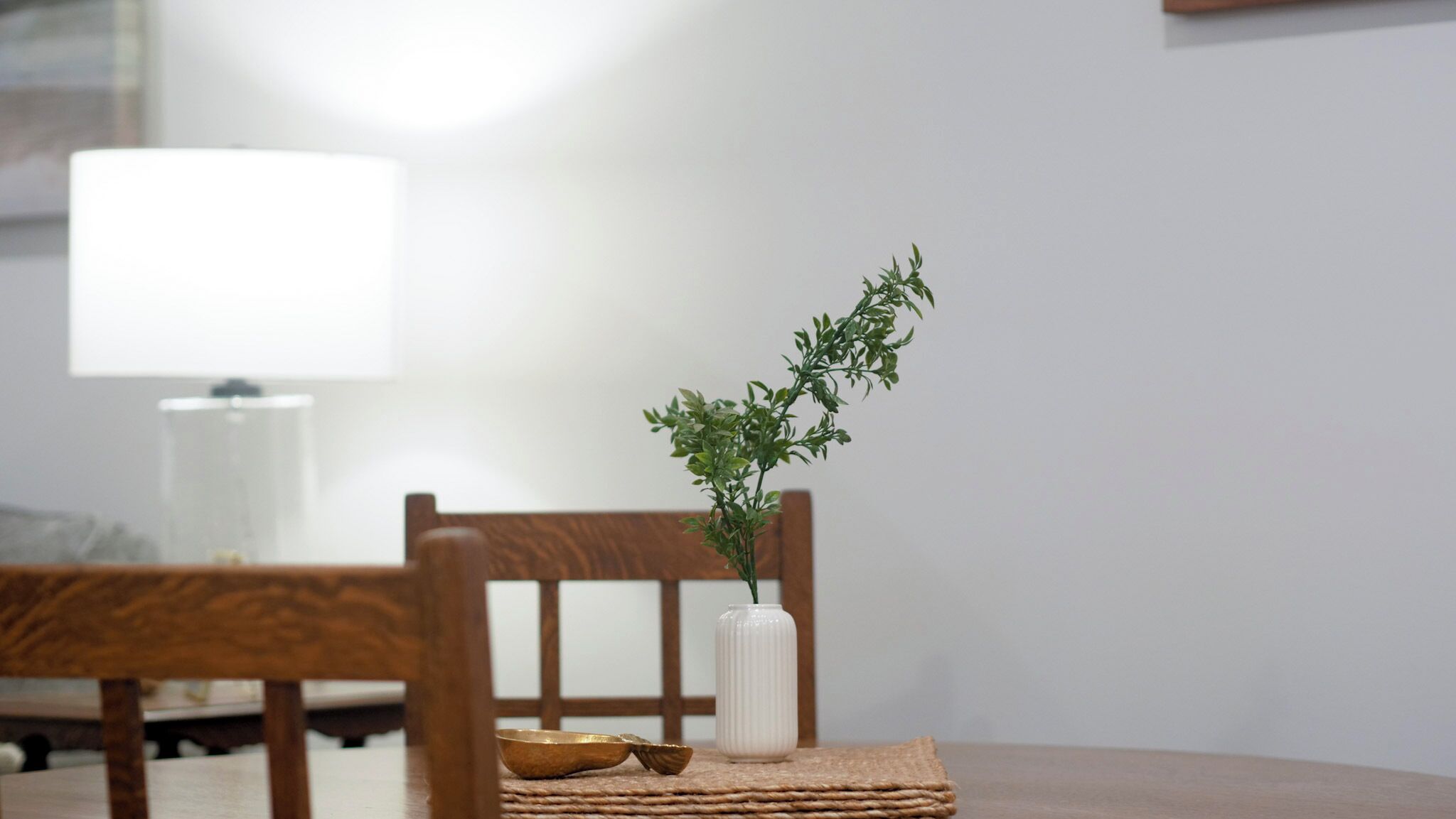 Un'area pranzo con una sedia in legno, un sottopiattino intrecciato, un vaso bianco con una pianta e una ciotola.
