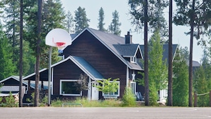 Ein zweistöckiges Haus mit Basketballkorb davor, umgeben von hohen Bäumen.