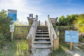 A wooden staircase leading to a beach area with signs indicating beach regulations and a pay-to-park sign.