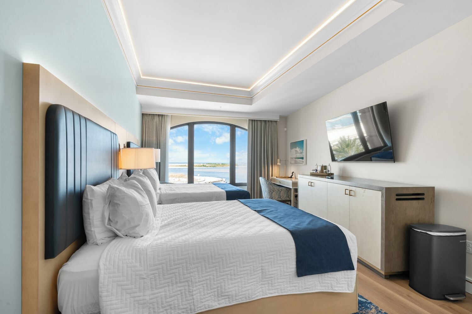 Une chambre d’hôtel avec un grand lit, un bureau, une télévision et une vue sur la mer.