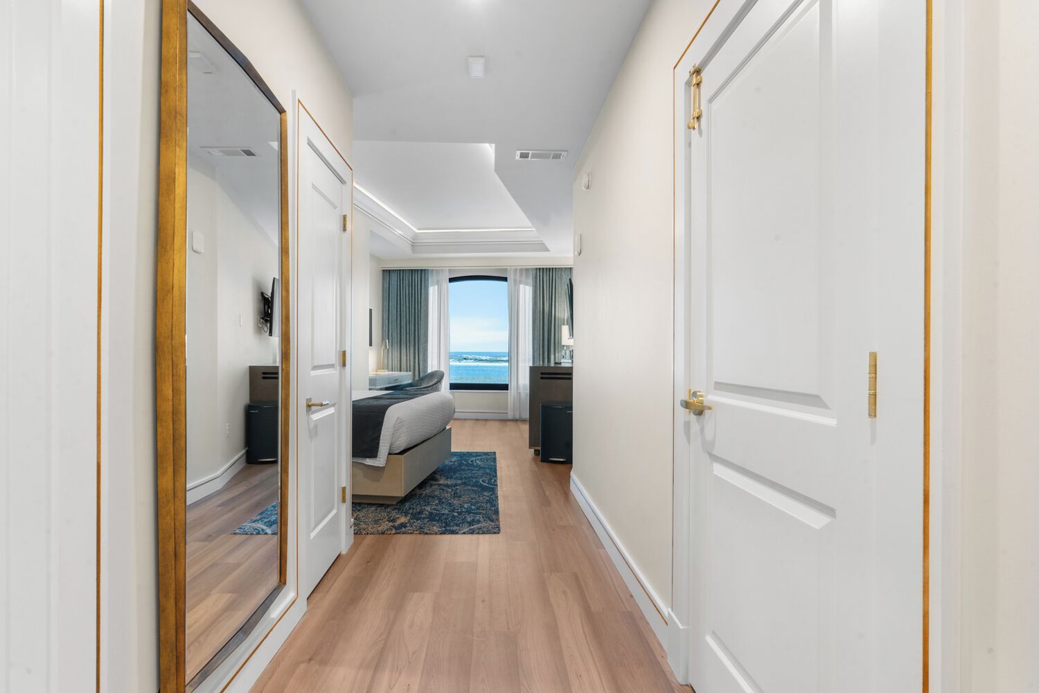 A hotel room with a bed, a desk, a chair, a TV, and a view of the sea.