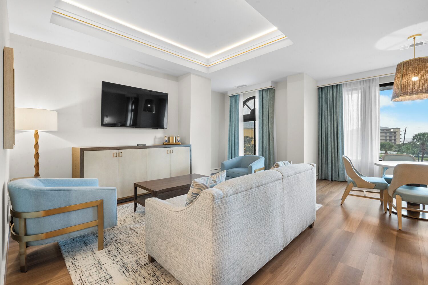 Una habitación de hotel moderna con sofá, sillas, una mesa de comedor, televisor y vistas a la ciudad.