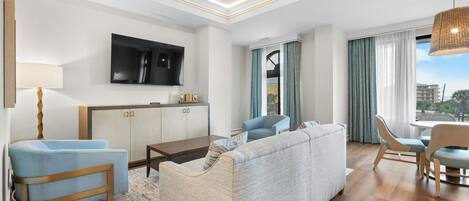 Una habitación de hotel moderna con sofá, sillas, una mesa de comedor, televisor y vistas a la ciudad.