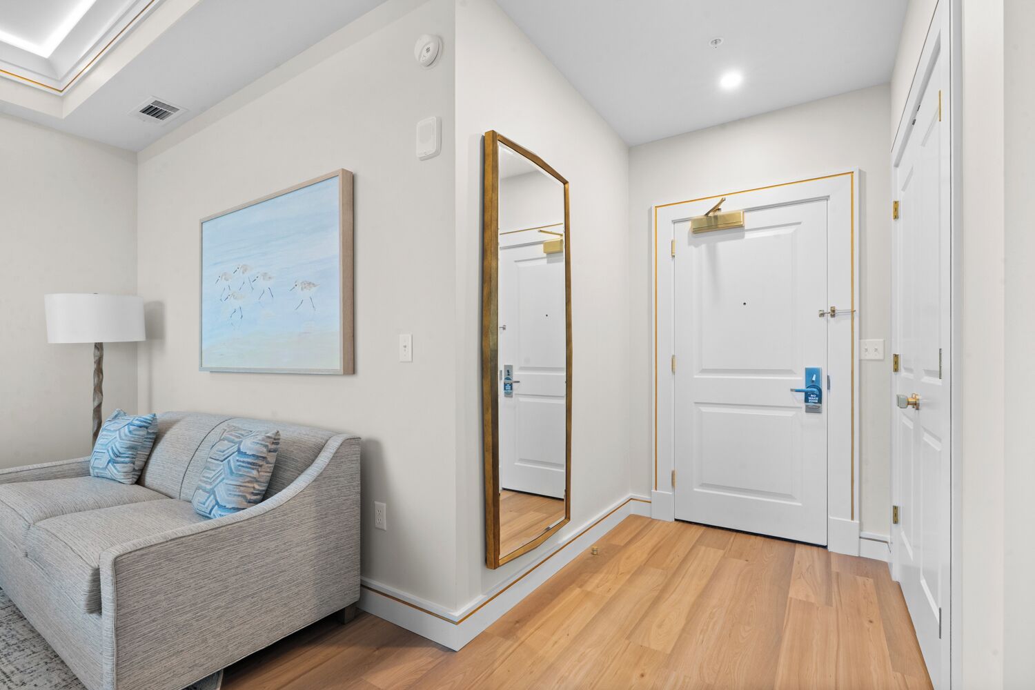 A modern bedroom with a grey sofa, a large mirror, and a door with a blue lock.