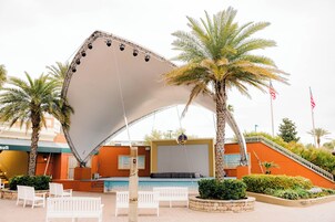 Un área junto a la piscina con una gran estructura de sombrilla blanca, palmeras y sillas blancas.