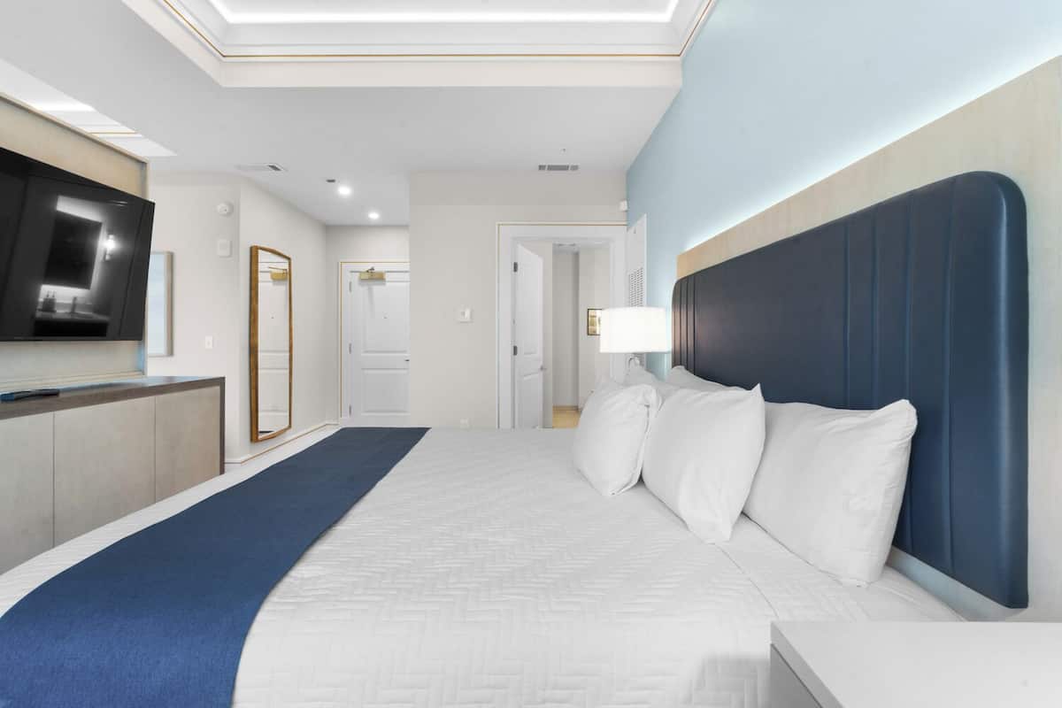 A modern hotel room with a large bed, a flat-screen TV, a desk, and a mirror.