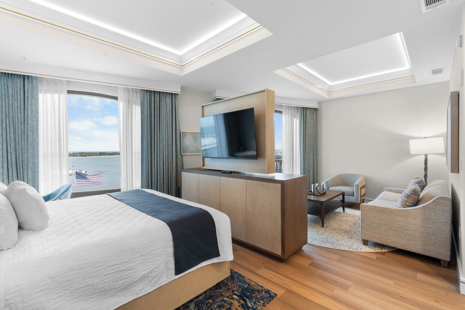 Una habitación de hotel con cama, escritorio, televisión, silla y vista al agua.