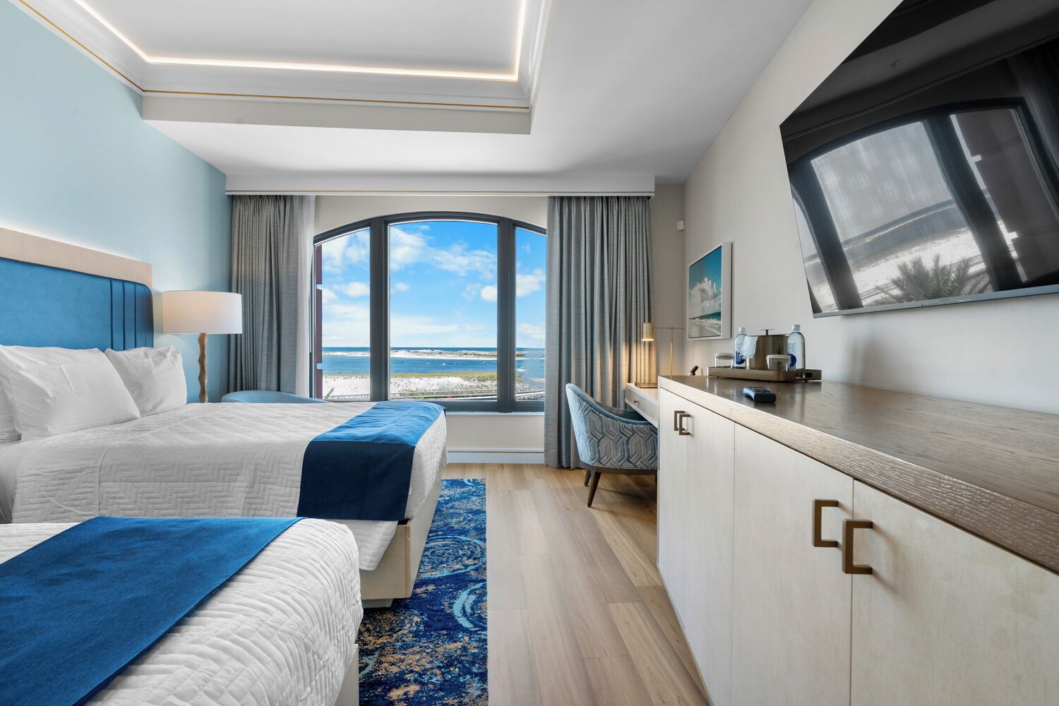 Camera d'albergo con due letti, una scrivania, una televisione e vista sulla spiaggia.