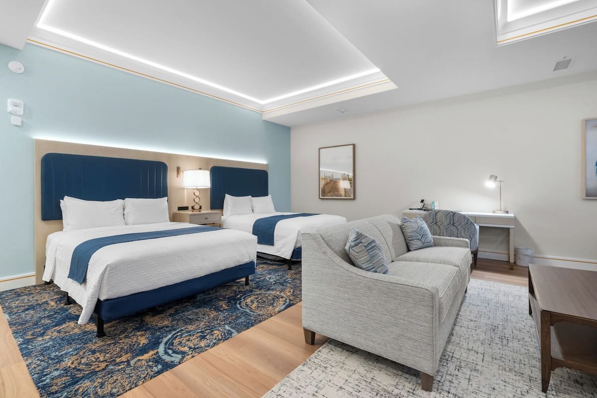 A hotel room with two beds, a sofa, a desk, and a large window.