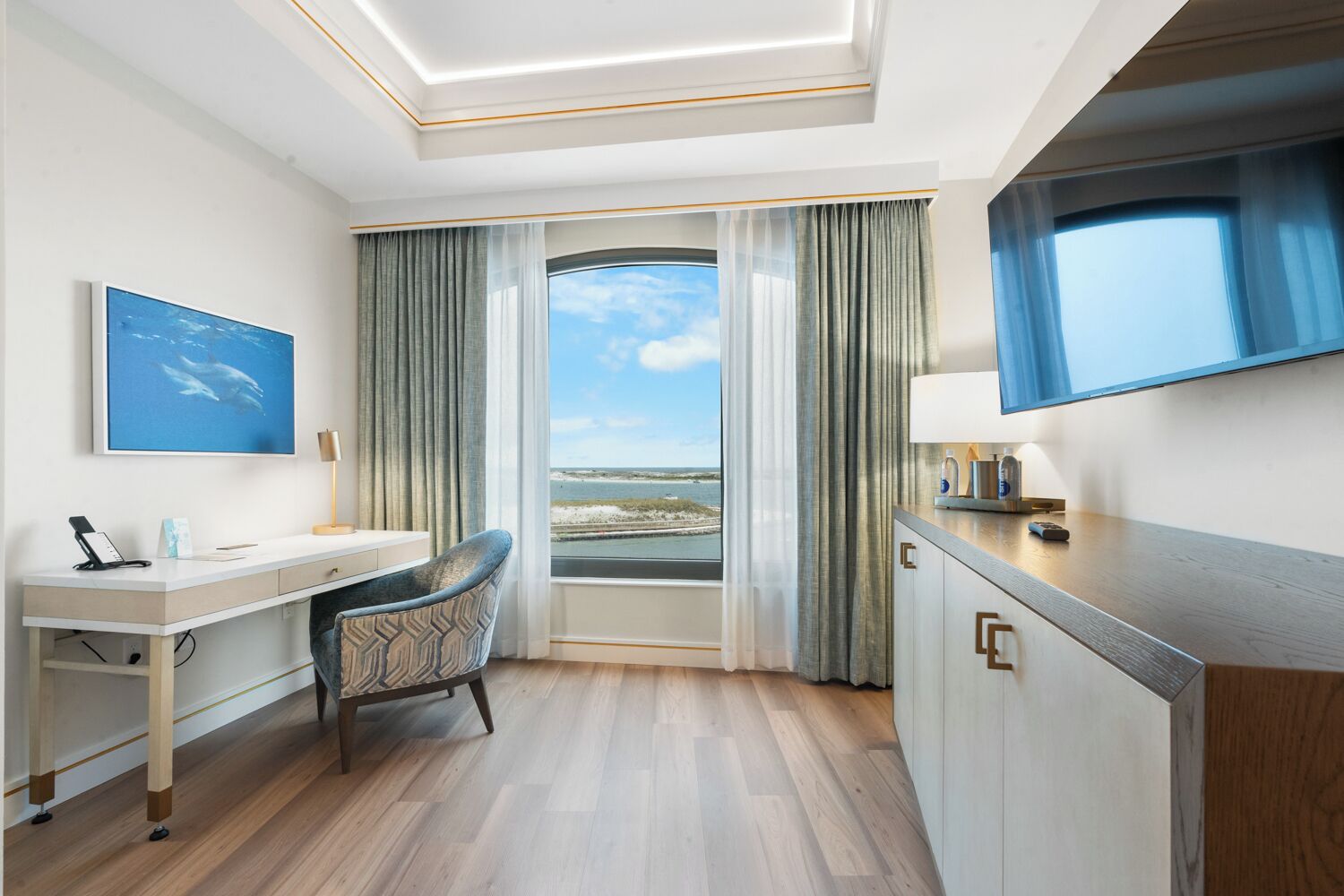 A hotel room with a desk, chair, and a large window offering a view of the beach.
