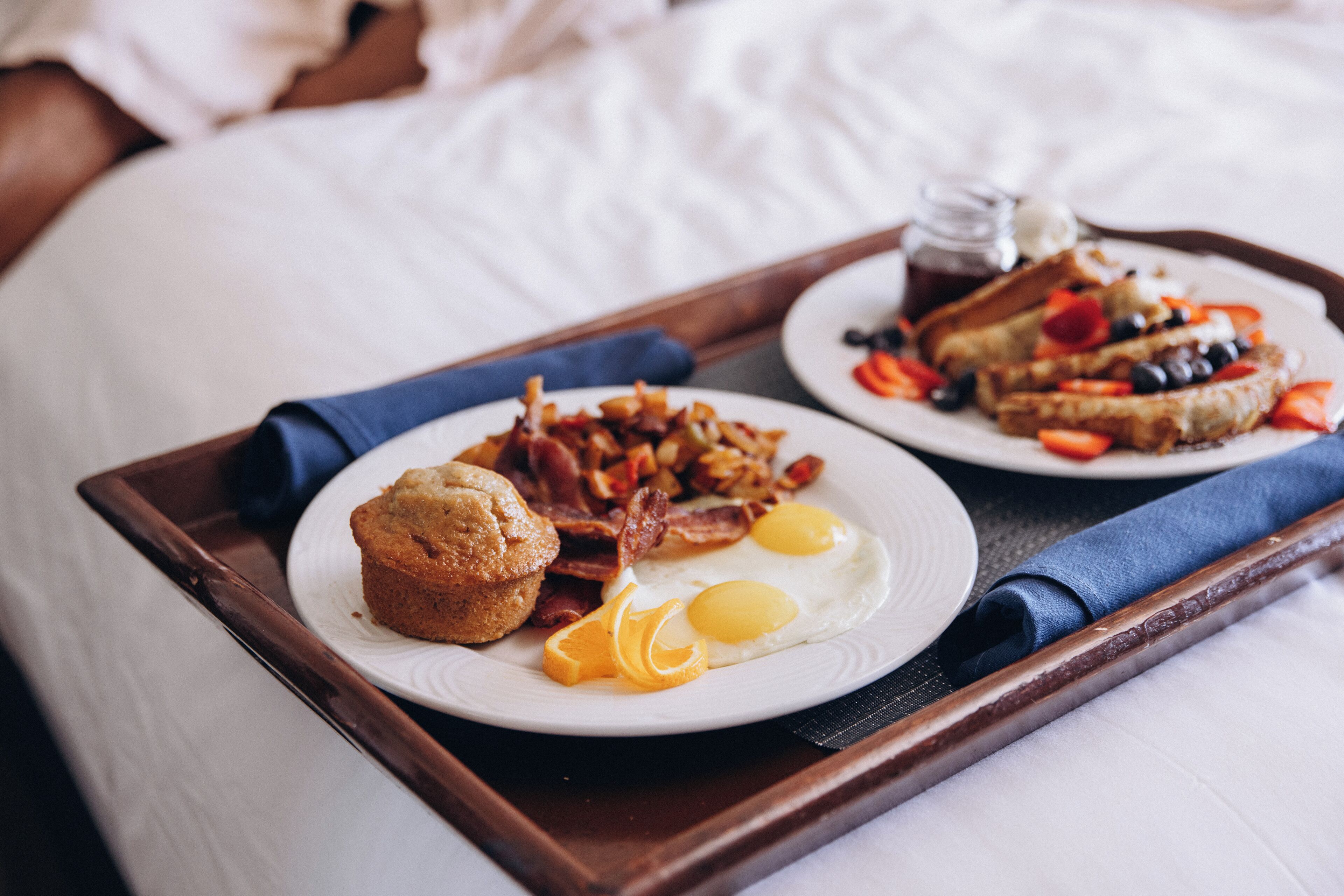 A breakfast tray with muffins, bacon, eggs, and toast on a bed.