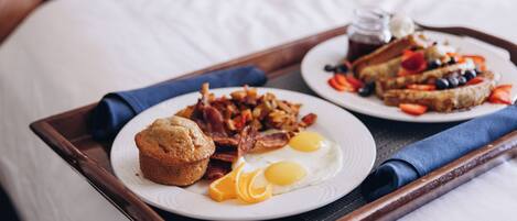A breakfast tray with muffins, bacon, eggs, and toast on a bed.