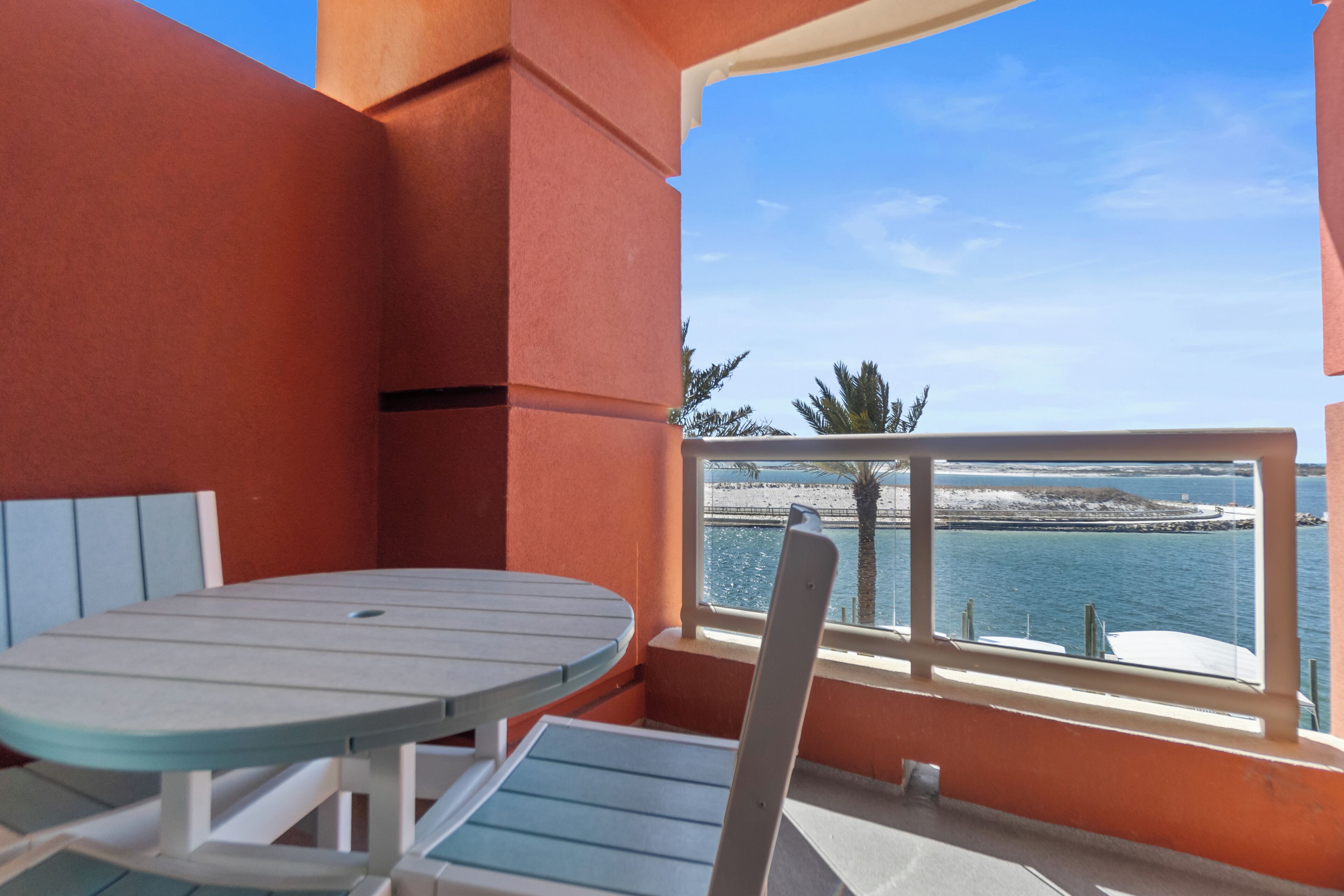 A balcony with a table and chairs, overlooking a coastal view.