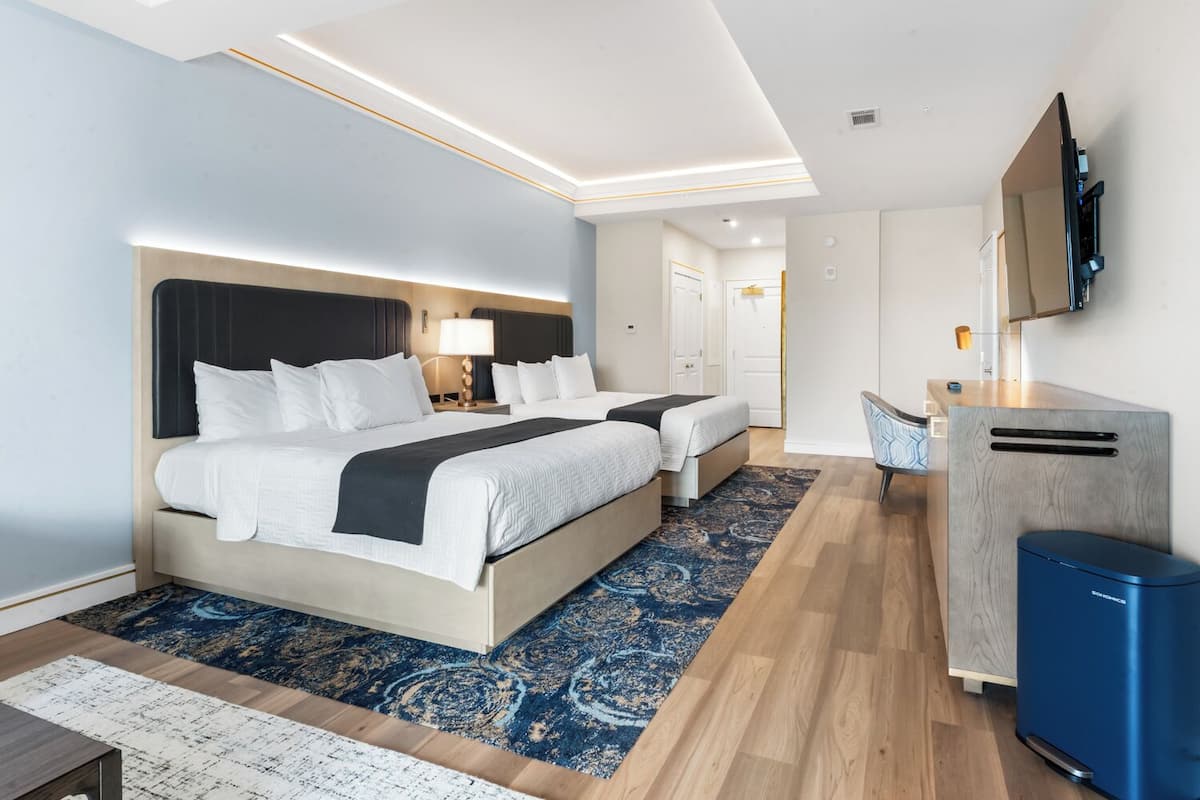 A modern hotel room with a large bed, bedside tables, a desk, a chair, a TV, and a wardrobe.