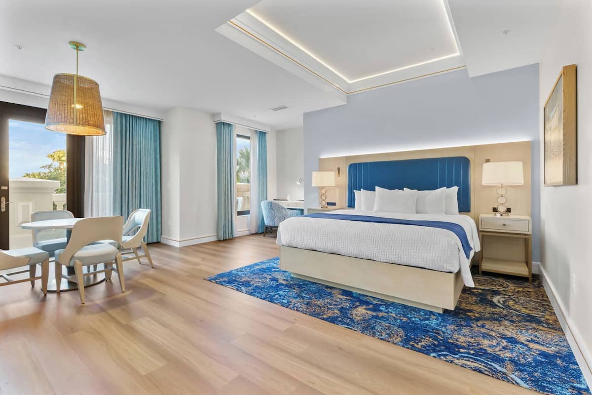 A modern hotel room with a large bed, a desk, and a dining area.