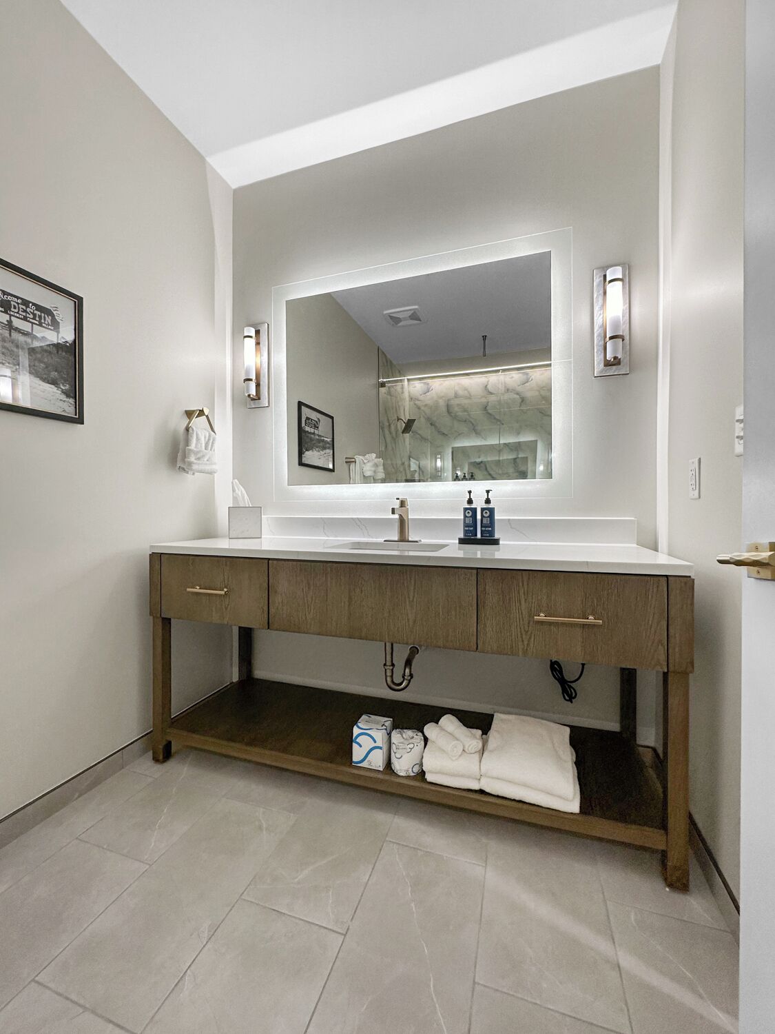 A modern bathroom with a large mirror, a white countertop, and wooden cabinets.