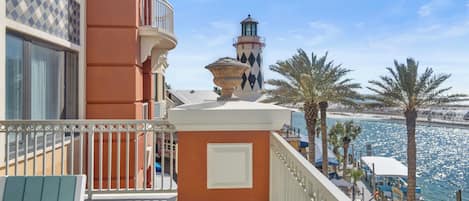 Un balcón con vistas al mar, un faro y palmeras.